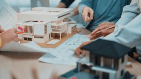 Professionals engage in a collaborative architecture design session, analyzing blueprints and a scale model in a modern office workspace, fostering creativity and teamwork. SACTR - Powered by Shutterstock - Get 15% off with code: PIKWIZARD15