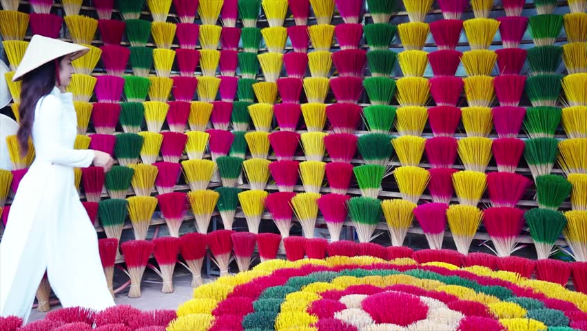 A young Vietnamese woman in a white national costume arranges colorful incense sticks in Hue, Vietnam.