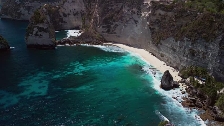 On a bright sunny day, drone footage captures the beauty of Diamond Beach Bali where the steep cliff walls rise above turquoise waters.