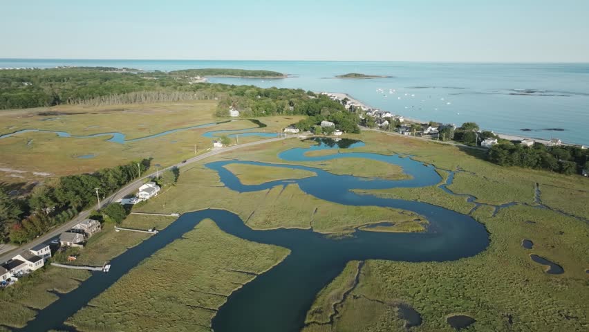 Aerial view of tidal marshes in Kennebunk, Maine, with winding waterways, beachfront homes, and the Atlantic Ocean stretching out under clear skies.