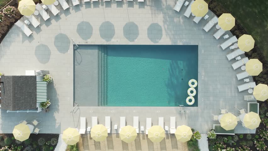 Aerial view of a modern hotel pool with bright yellow umbrellas, lounge chairs, and perfectly landscaped grounds—clean symmetry and luxury summer vibes.