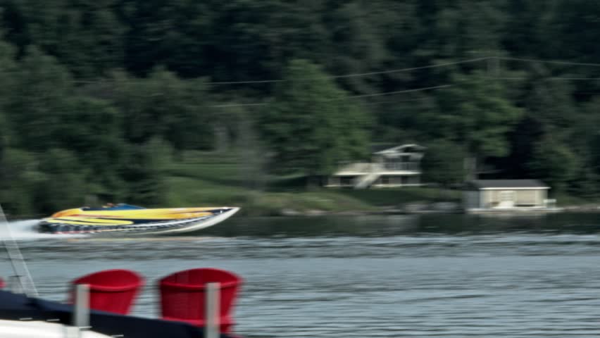Yellow power boat races along a tree lined river with rooster tail shooting up