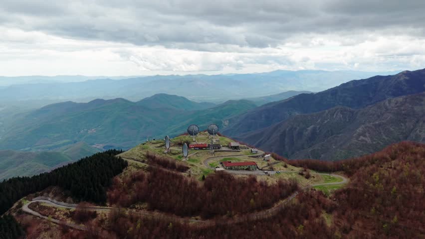 Old radar station on a remote mountaintop under cloudy skies, aerial view