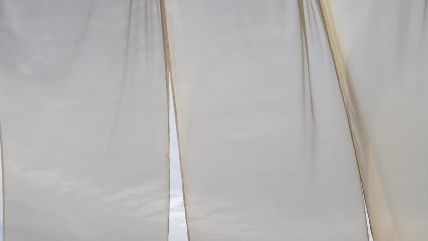 Light sheer curtain blowing in the wind with cloudy sky behind it