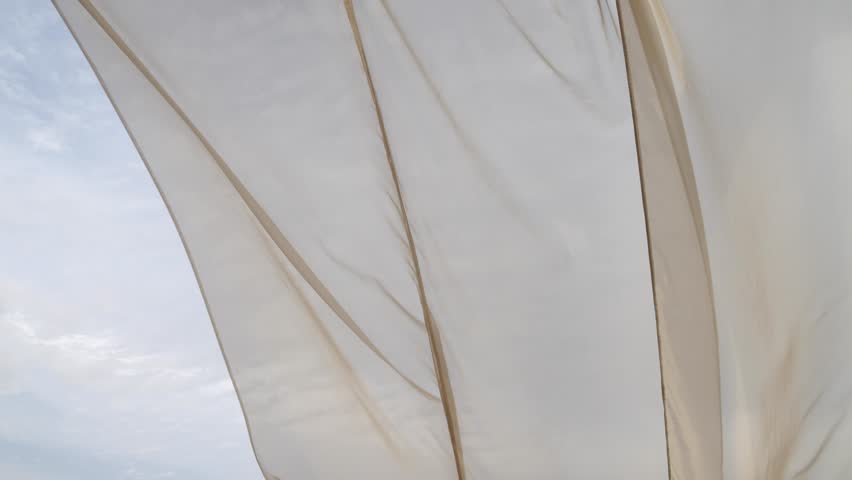 Light sheer curtain blowing in the wind with cloudy sky behind it