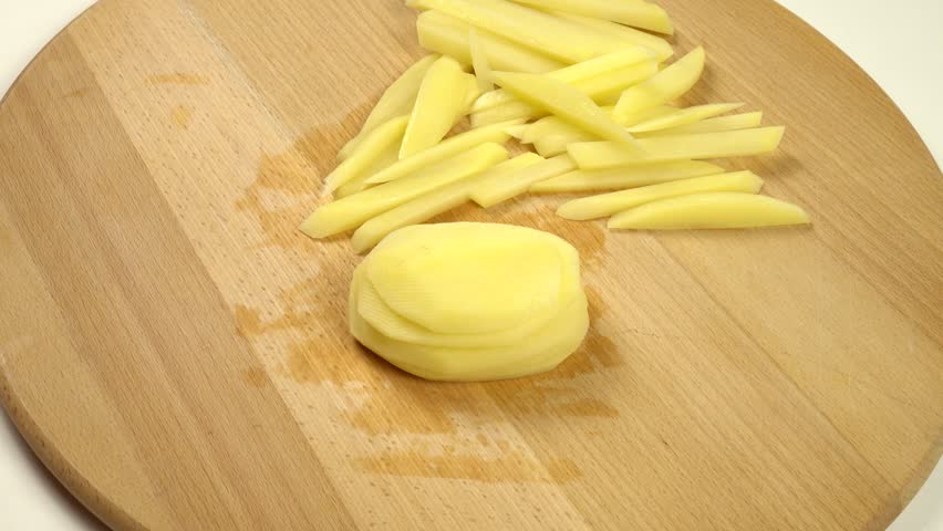 Cutting raw potatoes into strips on a cutting board to make French fries