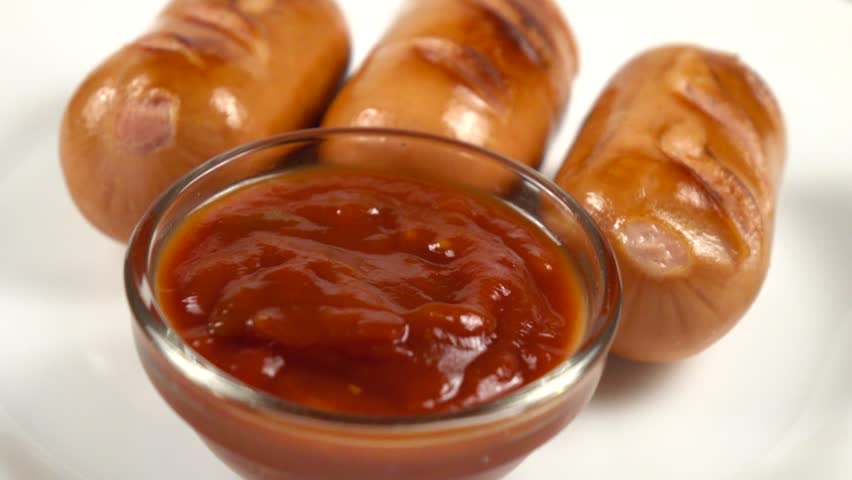 Grilled sausages and jar with ketchup are on a white plate, slow motion, homemade food 