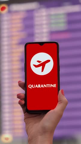 Closeup, woman, in protective mask, holds smartphone with airplane icon, quarantine sign, on screen, in front of flight information board in departures terminal, at airport.