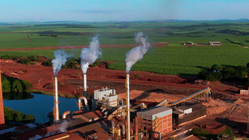 Drone aerial landscape of steam coming from turbines at Ethanol production plant factory with warehouse facility in farmland countryside region valley of Brazil South America industry processing