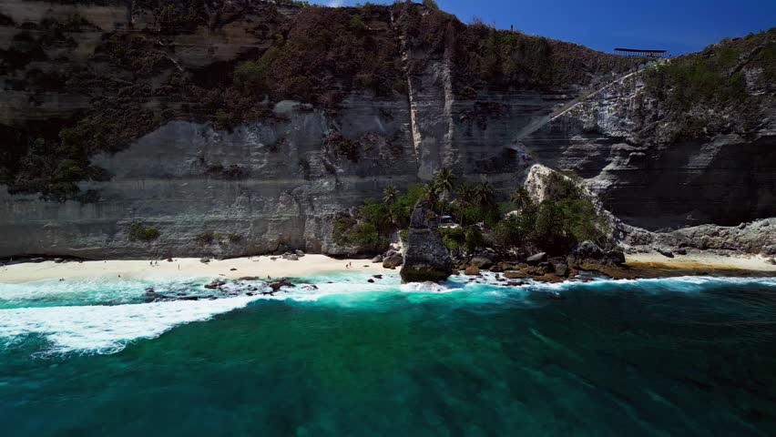 Diamond Beach in Bali, drone footage reveals a stunning view of sharp cliffs, turquoise ocean, and golden sunlight.
