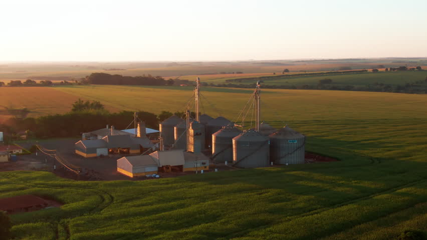 Grain silos on a farm at sunset, showcasing open fields and agricultural land, aerial view