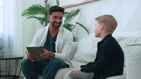 Indian Pediatric healthcare professional engaging young kid child boy patient, consulting with digital tablet during medical interaction inside hospital examination room - Powered by Shutterstock - Get 15% off with code: PIKWIZARD15