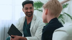 Friendly pediatrician reviewing medical details on digital tablet, communicating warmly with young kid boy patient during pediatric examination in well-lit healthcare setting - Powered by Shutterstock - Get 15% off with code: PIKWIZARD15
