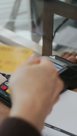 Vertical close-up shot of unrecognizable person making credit card payment on terminal and receiving receipt