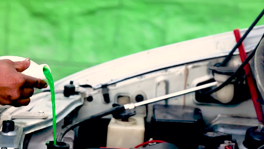Green fluid being poured into an open car engine under the hood. Concept of automotive service, coolant refill, vehicle care, and technical maintenance during repair or inspection.