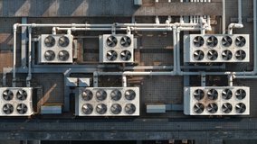 Aerial view of multiple cooling units situated on a rooftop. The system features a series of large HVAC units and extensive piping. - Powered by Shutterstock - Get 15% off with code: PIKWIZARD15