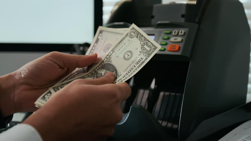 Close-up shot of unrecognizable hands using money counting machine on stack of American dollar bills