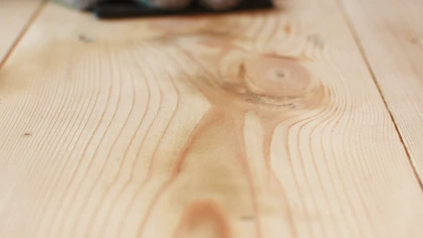Worker's gloved hand manually sands wood, removing old varnish left after machine sanding and revealing natural surface texture.