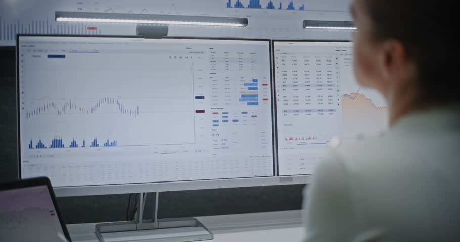 Female Financial Analyst Working on Computer with Multi-Monitor Workstation, Monitoring Real-Time Stocks and Exchange Market Charts. Successful Businesswoman Works in Investment Bank Office at Night.