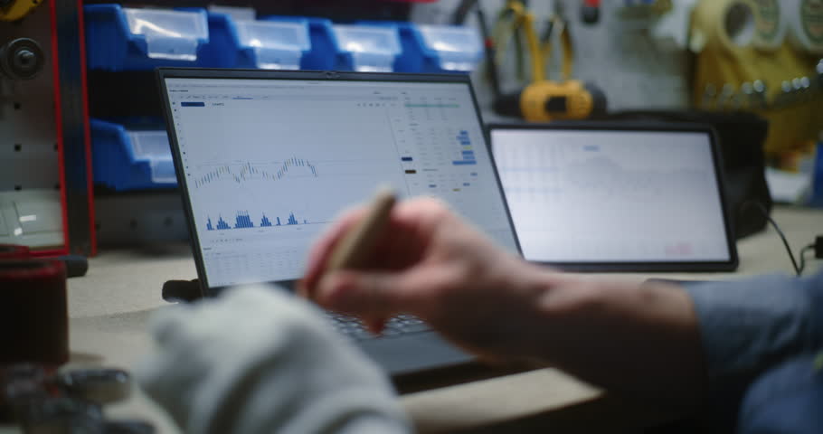 Craftsman Doing Handwork, Monitoring Stocks, Exchange Market Charts on Laptop and Tablet Computer. Man Making Investments During Working Day in Workshop, Combining Work with Online Trading. Close Up.