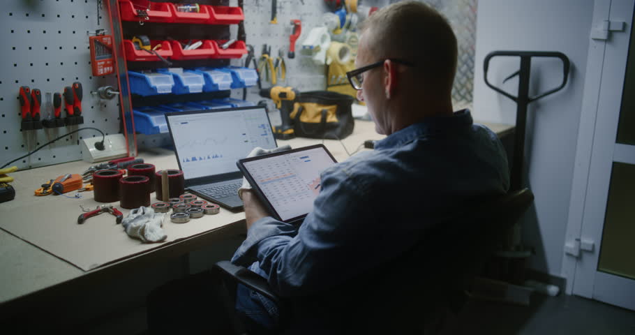 Employee Checking Real-Time Stocks and Exchange Market Charts Using Digital Tablet and Laptop. Man Making Cryptocurrency Investments During Working Hours in Workshop, Combining Job with Online Trading