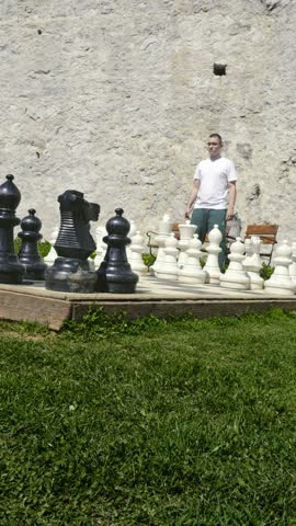A man intently plays giant chess outdoors, making his move with a white piece.