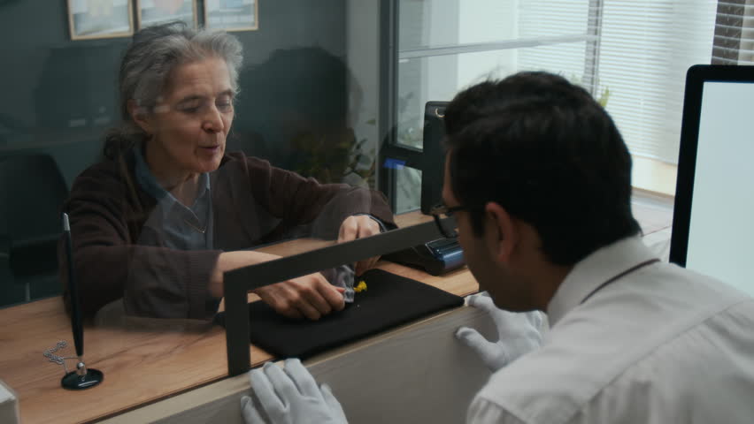 Over the shoulder shot of Indian gemologist carefully examining tiny gemstones with tweezers, brought by elderly woman in jewelry store