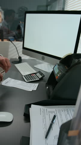 Vertical shot of unrecognizable bank worker using money counting machine on stack of American dollar bills in bank office