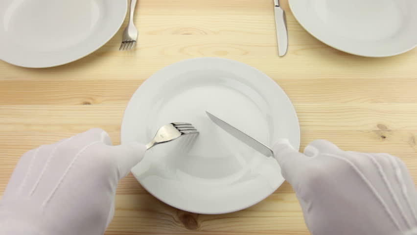 Wooden table. White plate. Hands in white gloves with a fork and a knife cut a