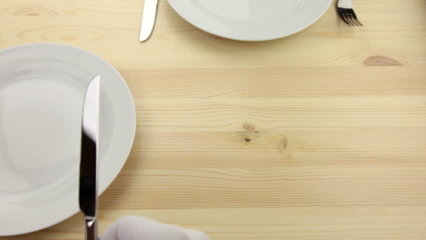 Wooden table. White plates. Hands waiters in white gloves, put a knife and fork
