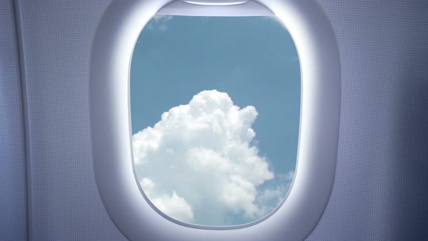 Airplane window. Behind him on a bright blue sky, white clouds float
