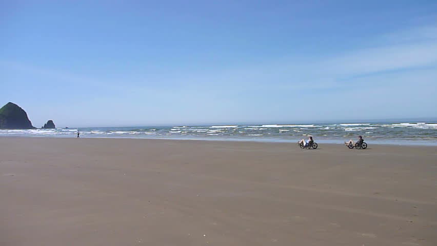 Man and woman riding bikes at Cannon Beach, Oregon on sunny day.