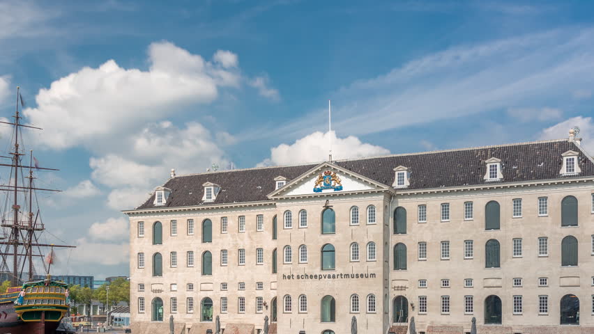 Hyperlapse of the National Maritime Museum with the sailboat replica Amsterdam docked nearby. Blue sky with clouds timelapse. Famous for cultural activity, canals and bridges. Amsterdam, Netherlands