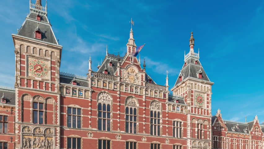 Hyperlapse of Amsterdam Central Railway Station with a historic building entrance. Many passengers moving in and out timelapse. Clouds in a blue sky. Amsterdam, The Netherlands