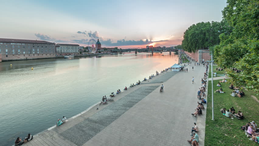 Aerial view of Port de la Daurade park along the Garonne River day to night transition timelapse in Toulouse, France. La Grave Hospital with Saint-Pierre Bridge during sunset with colorful clouds