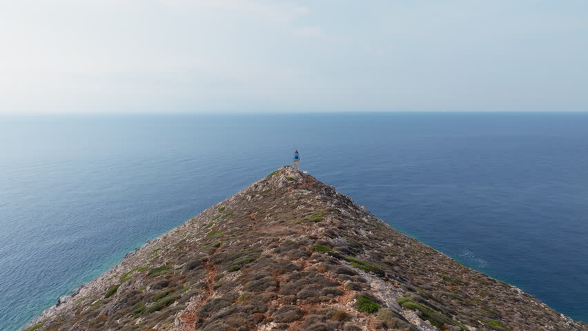 Aerial tracking shot reveals Cape Tainaron lighthouse closeup view on rocky coastline at the end of Mani Peninsula, Peloponnese, Mediterranean sea