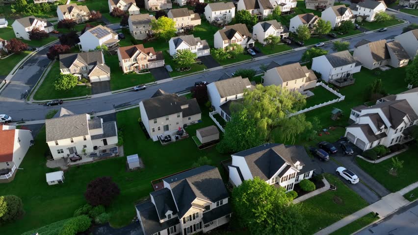 Two-story american one family houses with garden and double garage in quiet american neighborhood. Sunset time with green trees in spring. Suburb district located on hilltop on the evening. Aerial.