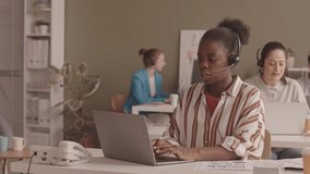 Waist up slowmo of young African American woman and her female colleagues working at call center in office, speaking to clients through headsets and entering data on laptops - Powered by Shutterstock - Get 15% off with code: PIKWIZARD15