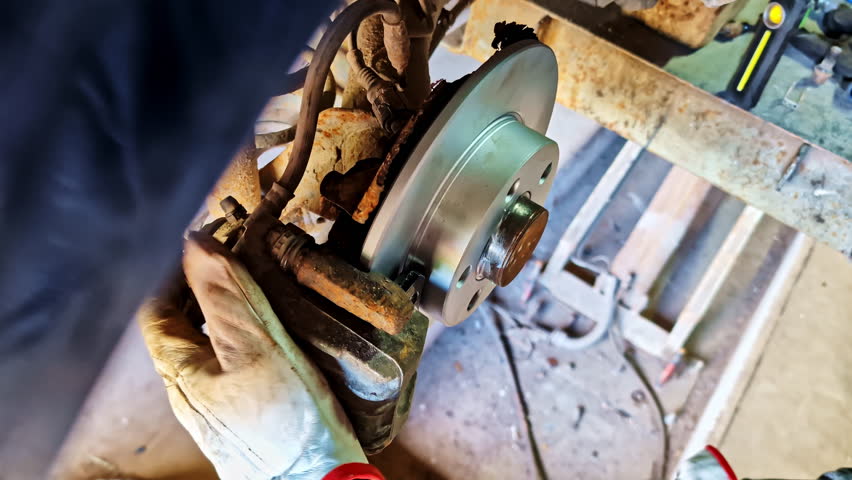 Mechanic installing new rear brake disc on rusted vehicle axle during maintenance