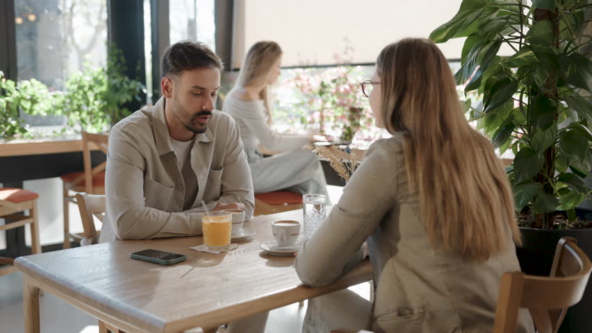 Friendly couple sharing warm conversation over refreshing beverages, enjoying casual interaction in modern urban cafe with natural light streaming through window