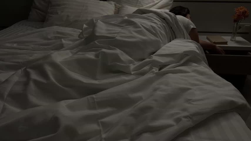 Woman preparing to sleep and putting on a sleep mask in bed in hotel
