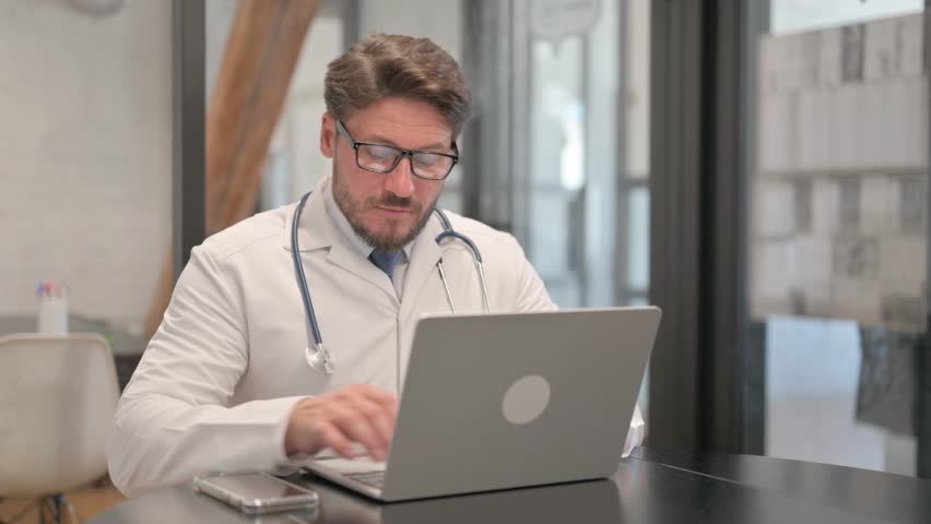 Young Doctor Typing on Laptop in Clinic