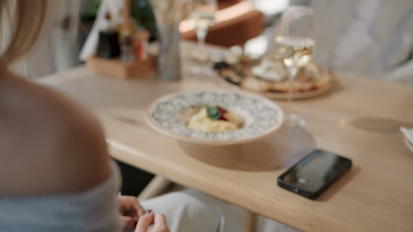 Video capturing female customer photographing gourmet pasta dish using smartphone while dining in trendy restaurant interior, showcasing modern food photography culture