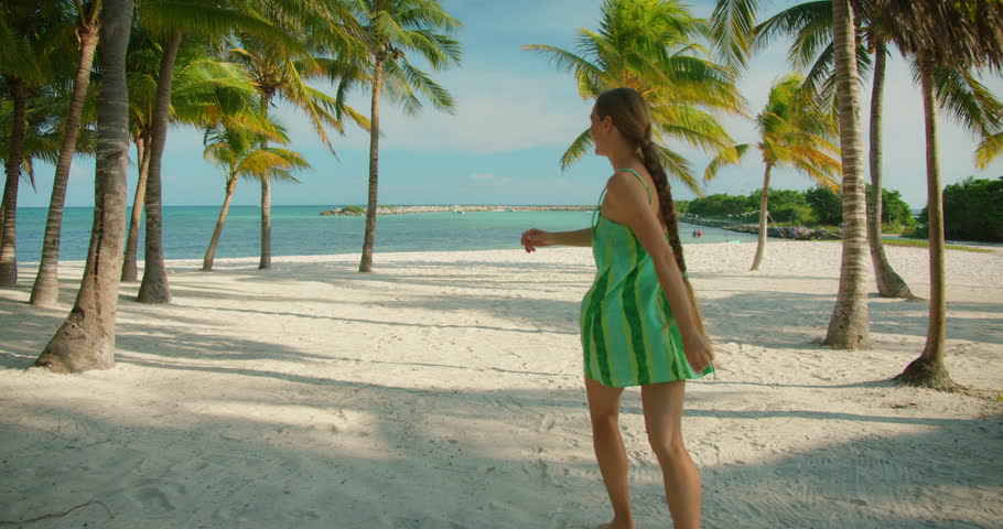 Woman runs barefoot on tropical beach surrounded by palm trees and sea in sunny day