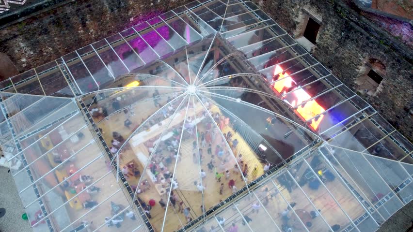 Smooth zoom out and slight pan to the left, gradually revealing the surrounding ruins and an open area with people enjoying the festive atmosphere inside a historic structure.