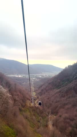 Cable car gliding over Shahdag’s forested valley with mountain views and distant townscape. Shahdag, Azerbaijan