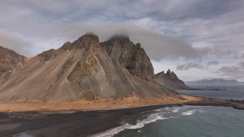 Vestrahorn and Brunnhorn rise over black beach and crashing waves on Iceland