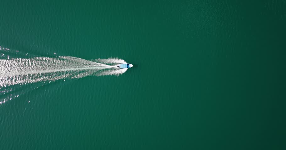 Aerial view of a lone boat slicing through green water, leaving a sharp wake across Lake Petén Itzá, Guatemala.