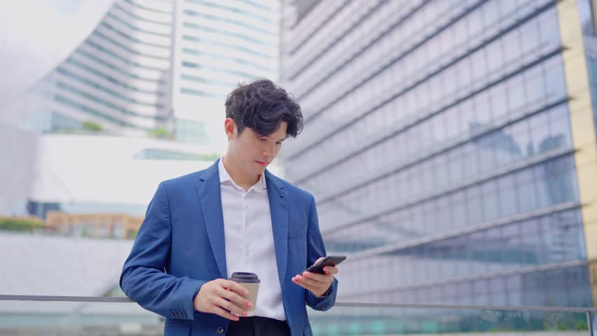 Asian young businessman chatting on smartphone while standing in city. Attractive handsome male employee worker communicate and discuss on mobile cellphone with colleagues outdoors with confidence. - Powered by Shutterstock - Get 15% off with code: PIKWIZARD15