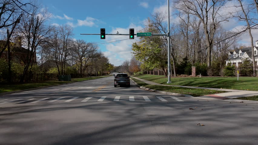 POV outside shot from the car moving along the small town streets with green traffic light at sunny day. Warm beautiful pictures of neighborhoods. 